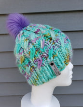 Load image into Gallery viewer, Cable effect beanie in teal with speckles of purple, yellow, and pink. Purple pom on top.