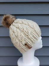 Load image into Gallery viewer, Ivory cable effect beanie with tan faux fur pom on top.