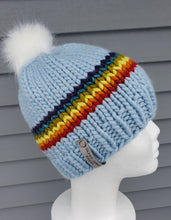 Load image into Gallery viewer, Classic beanie features a lovely rainbow stripe on sky blue background with a cloud-white faux fur pom on top.