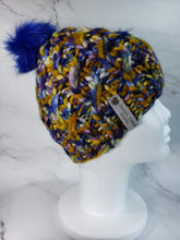 Load image into Gallery viewer, Cable effect beanie in a multicolor yarn with Navy blue, yellow and hints of purple topped with a bright blue pom.
