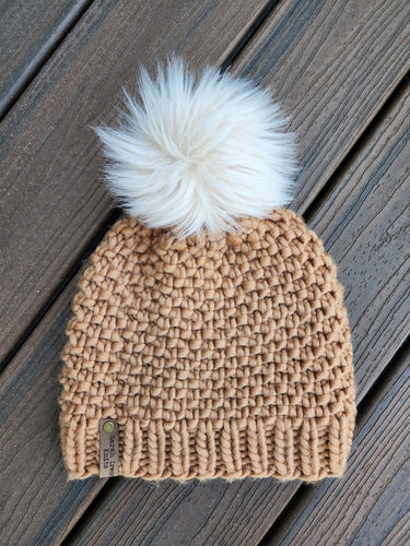 Tan colored textured beanie with ivory faux fur pom on top.