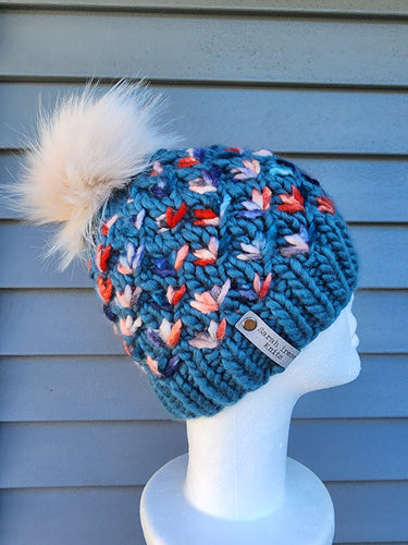 Light teal beanie with red, orange, blue multicolor flower pattern. Topped with ivory faux fur pom.