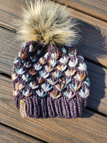Brown beanie with green and tan multicolor flowers. Topped with a tan lux pom.