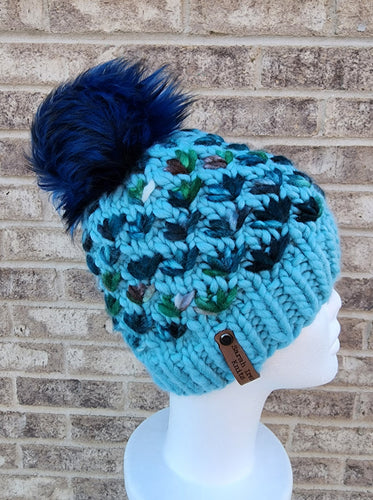 Light blue beanie with multicolor blue flower stitching. Topped with large luxury faux fur pom in dark blue.