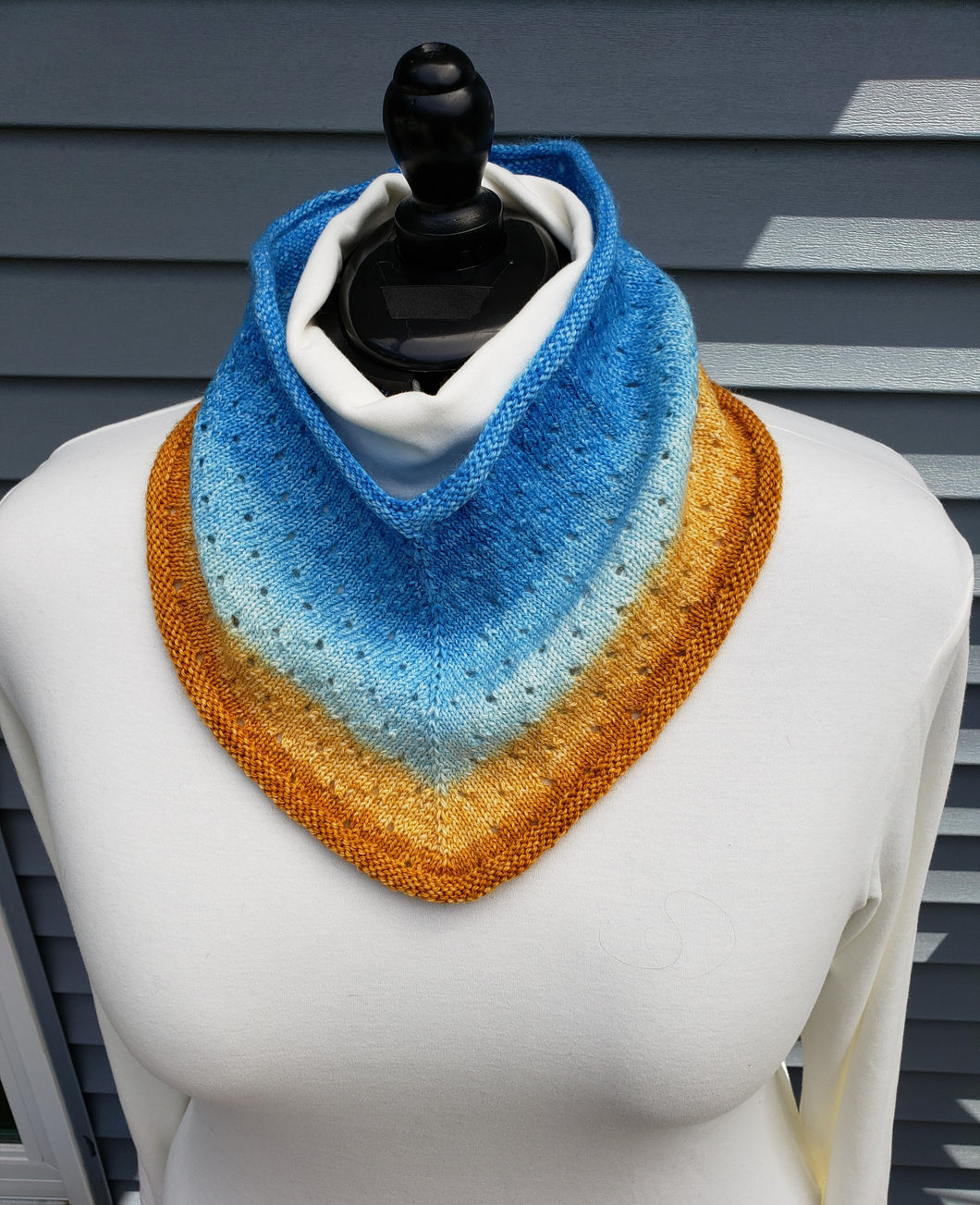 Cowl with eyelets in a gradient yarn from Blue at top to lighter blues then yellows and orange at bottom.