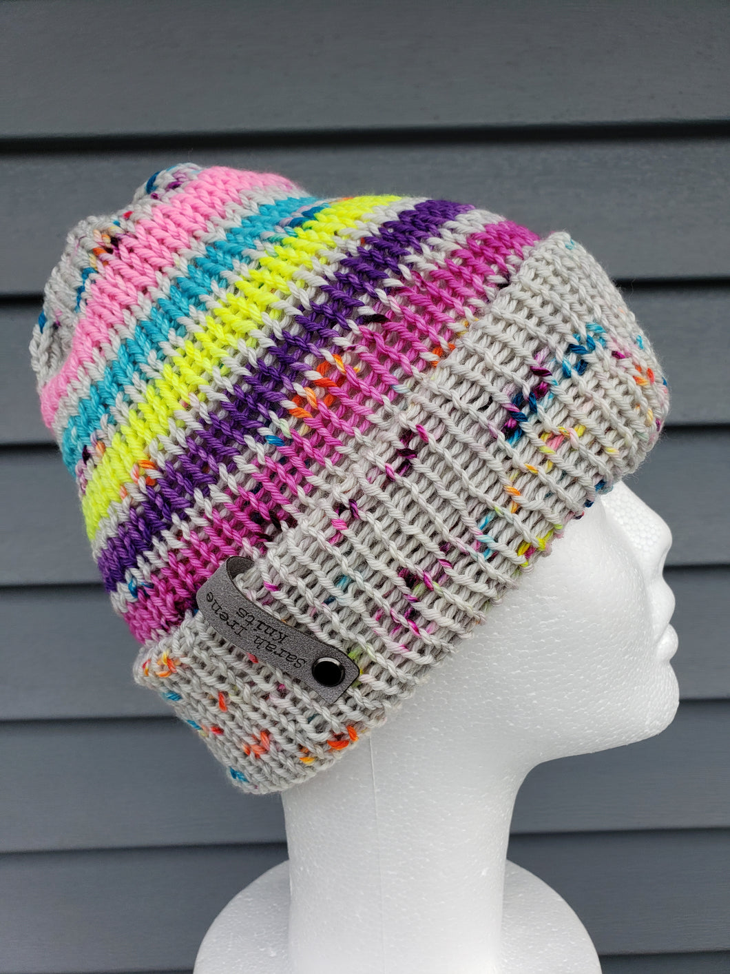 Double brim beanie in stripes of neon colors alternating with grey speckled bands. No pom.