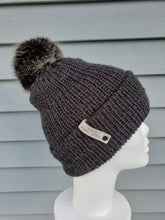 Load image into Gallery viewer, Charcoal colored double-brim beanie with a dark faux fur pom on top.
