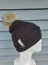 Load image into Gallery viewer, Charcoal colored double-brim beanie with a tan faux fur pom on top.
