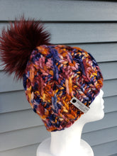 Load image into Gallery viewer, Cable effect beanie in orange, mauve, and blue multicolor. Topped with a large lux faux fur pom in burgundy.
