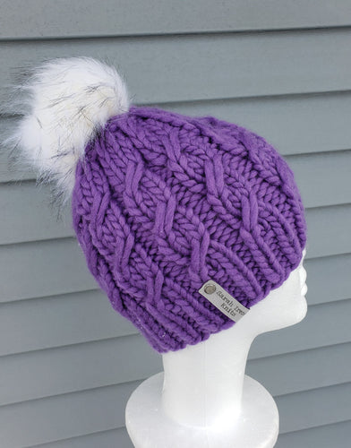 Bright purple cable effect beanie topped with a white faux fur pom.