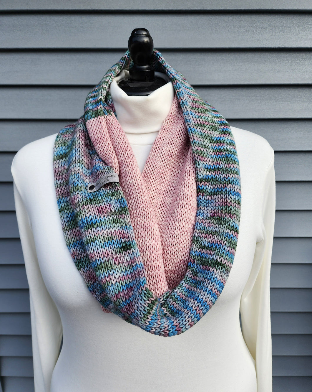 Infinity scarf in multicolor yarn with blues, greens, and pinks plus a block of solid pink yarn.