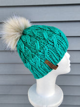 Load image into Gallery viewer, Braided effect beanie in subtle two-tone teal green color, topped with a large faux fur pom in ivory color.
