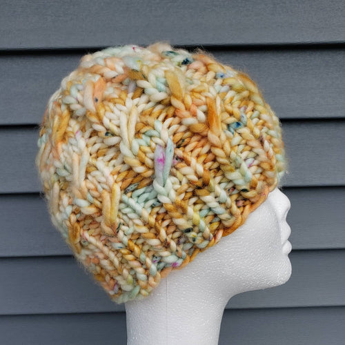 Cable effect beanie in a multicolor yarn with shades of tan, orange, yellow, blue, pink and more. No pom.